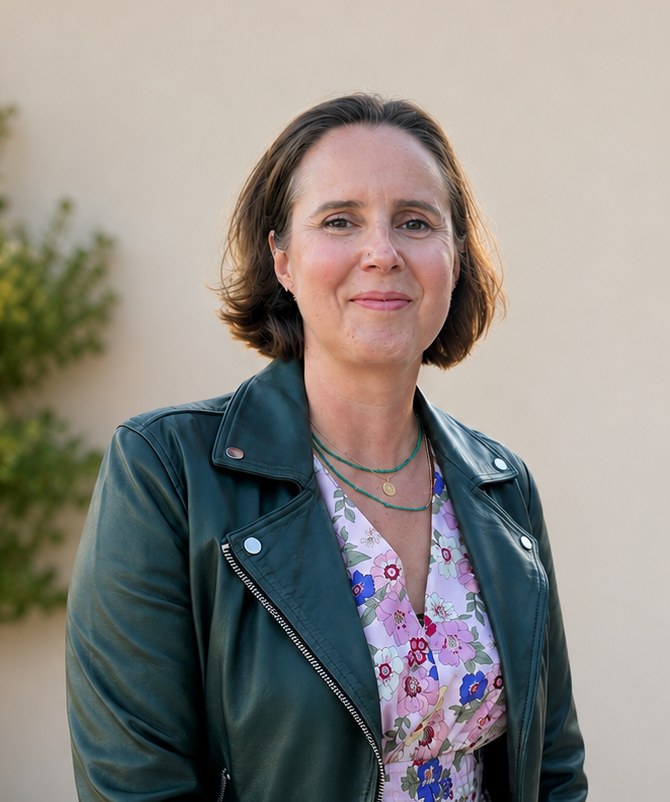 Miranda Gowlland smiling, wearing a green leather jacket, against a cream wall