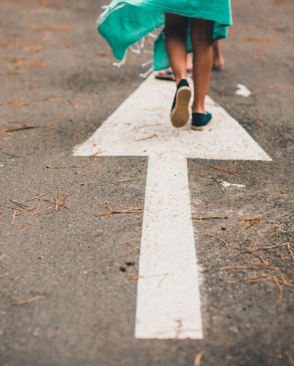 A woman in a green dress walking along a white arrow painted on a road